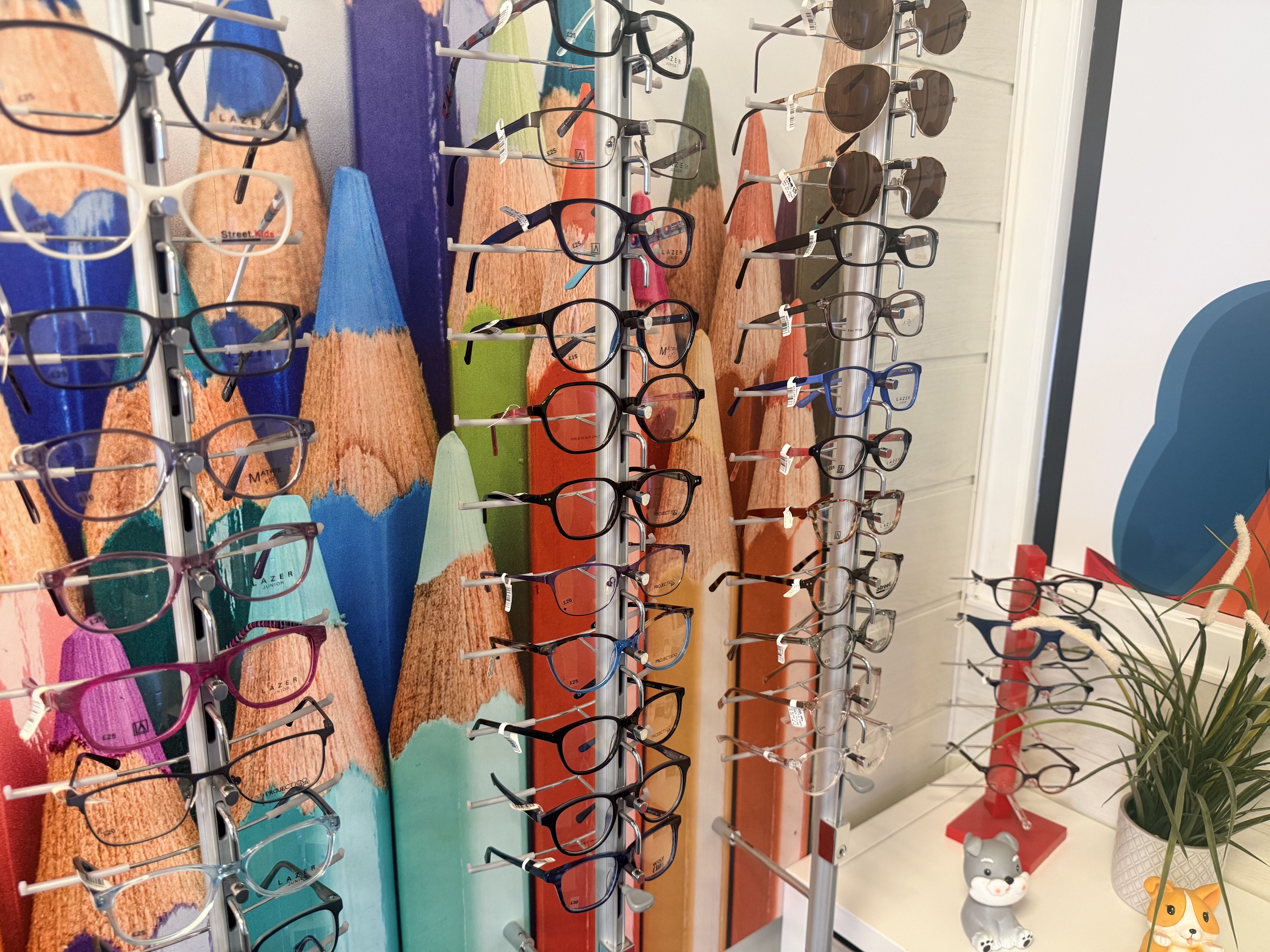 Display of eyeglasses and sunglasses organized on multiple rotating stands in optical store.