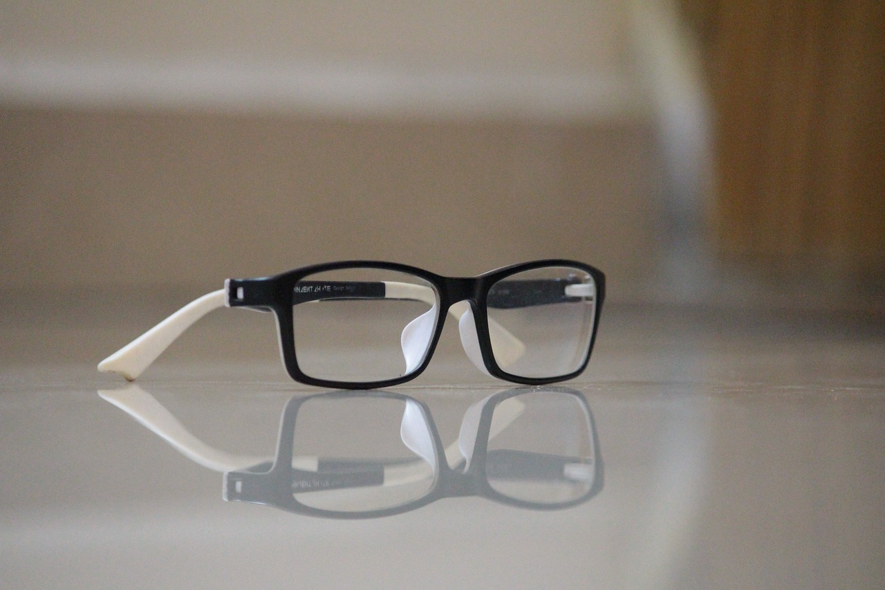 Black and white reading glasses with clear lenses casting shadow on reflective surface