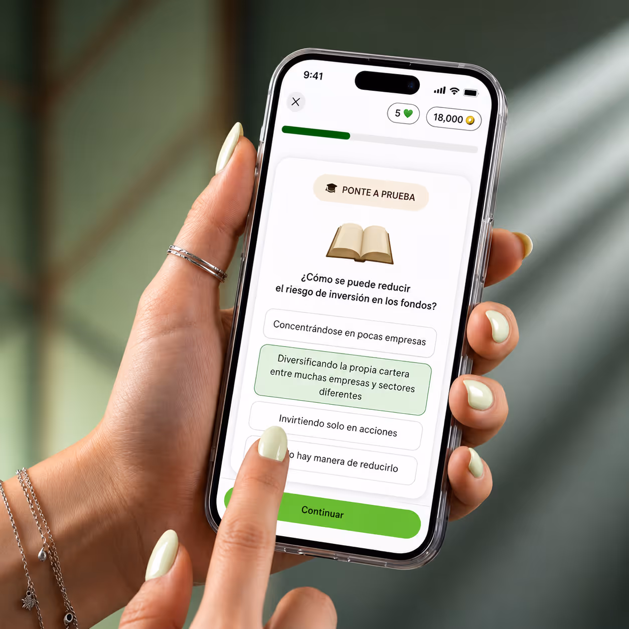 Mano con uñas verdes que sostiene un smartphone con una aplicación de bienvenida en Finanz, con texto en italiano y una imagen de un gato vestido leyendo un periódico.