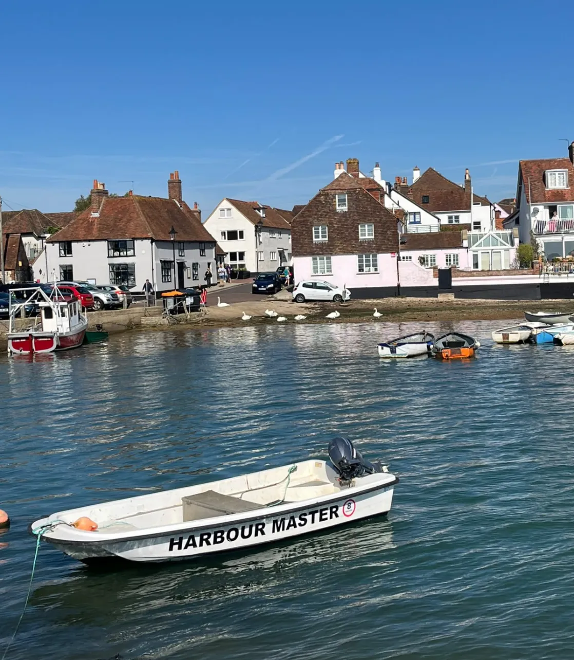 Image of Emsworth harbour, a small boat floating in the water in front of a street full of white town houses.