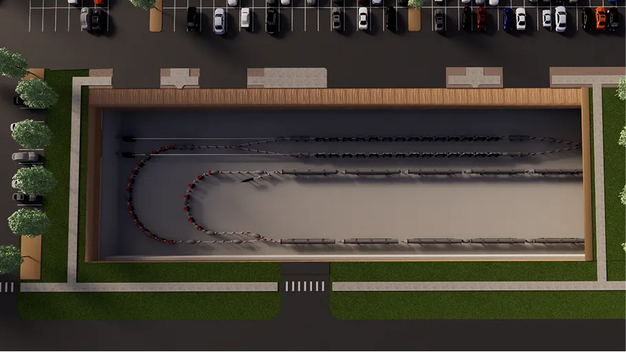 Top-down view of an electric vehicle charging station with multiple electric cars lined up and connected to chargers inside a rectangular building beside a parking lot.