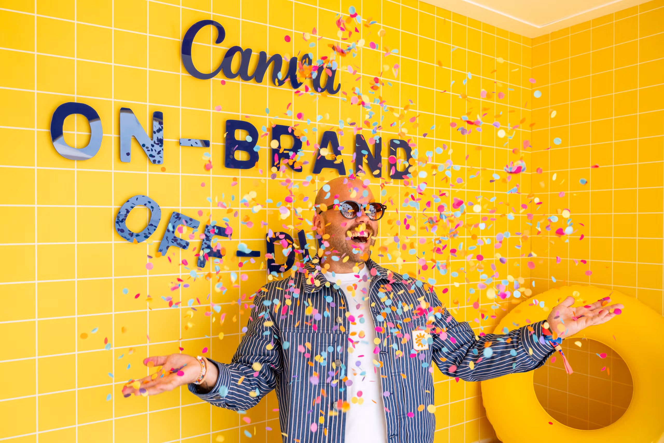 A guest with arms outstretched as confetti falls in front of the yellow tiled on-brand, off-duty wall at the Canva Creative Cabana.