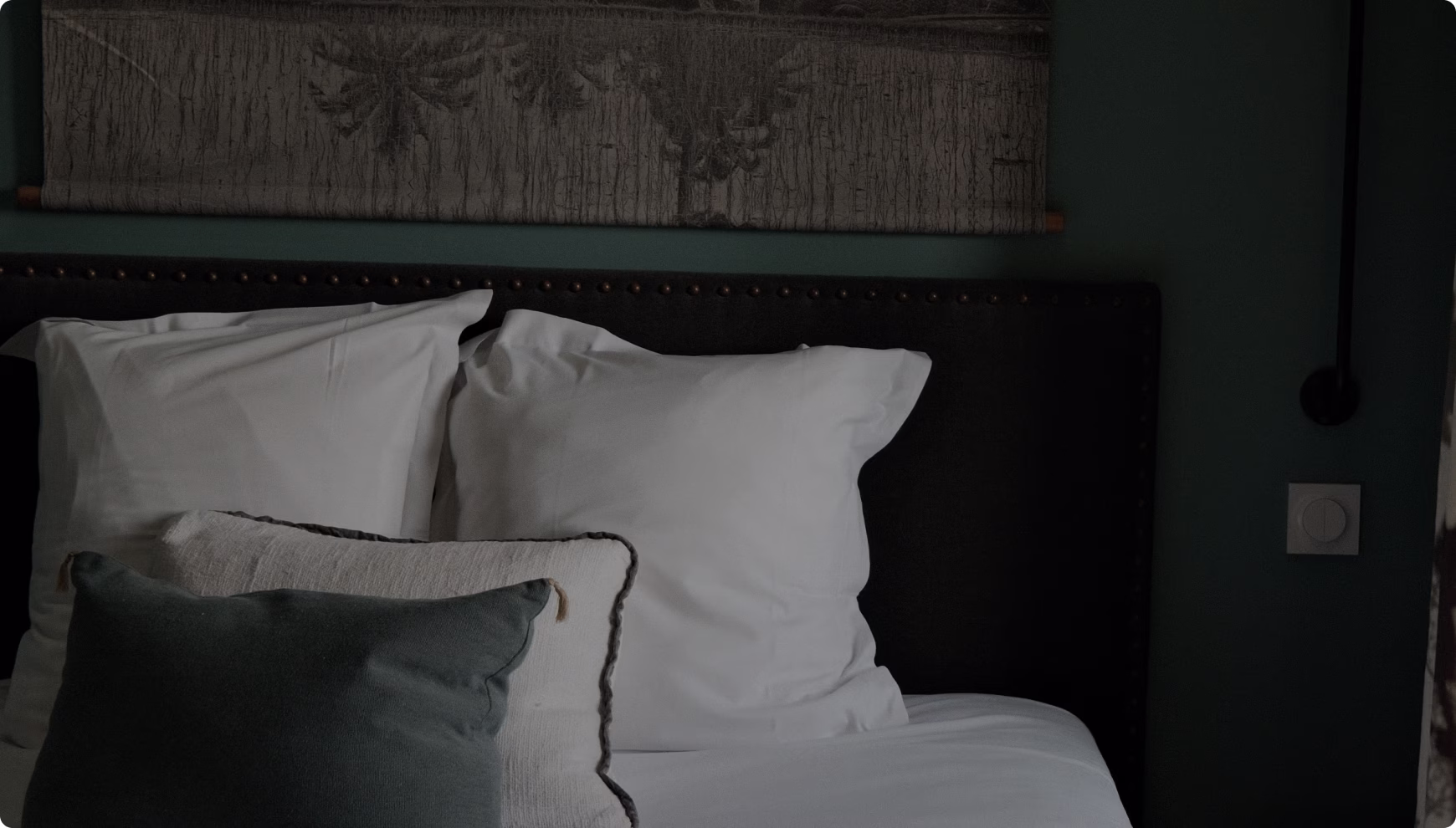 Lit avec deux grands oreillers blancs et un coussin décoratif vert dans une chambre à ambiance sombre.