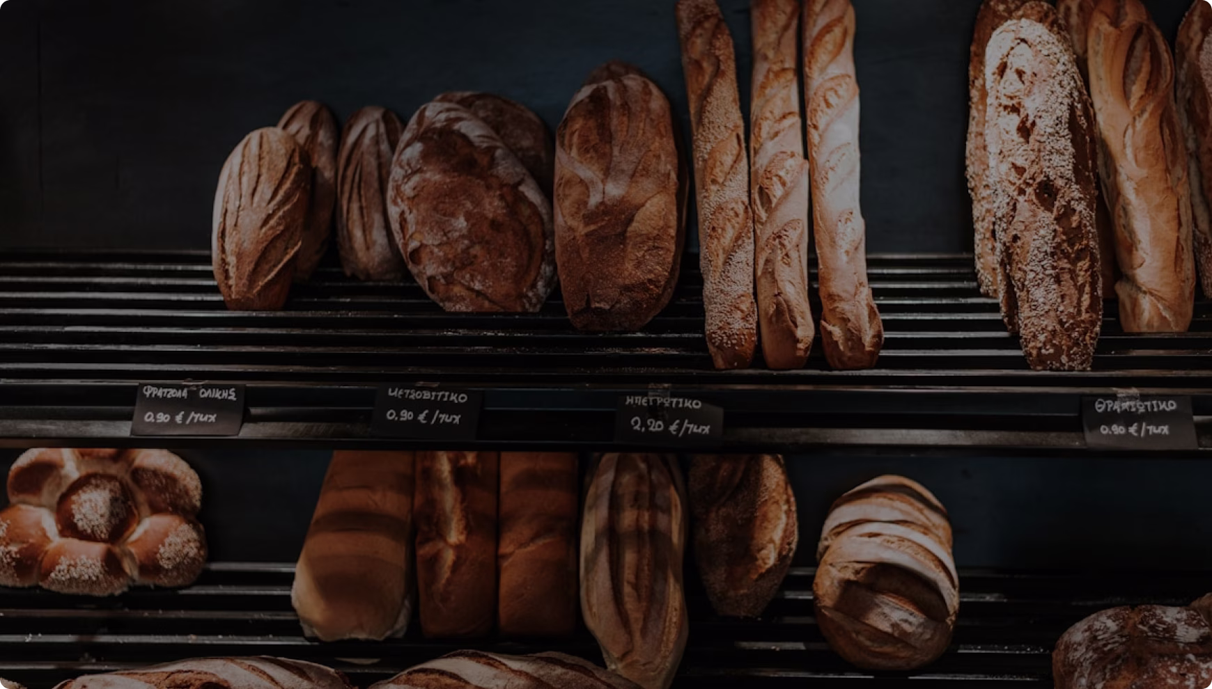 Différents types de pains artisanaux exposés sur des étagères de boulangerie avec des étiquettes de prix en euros.