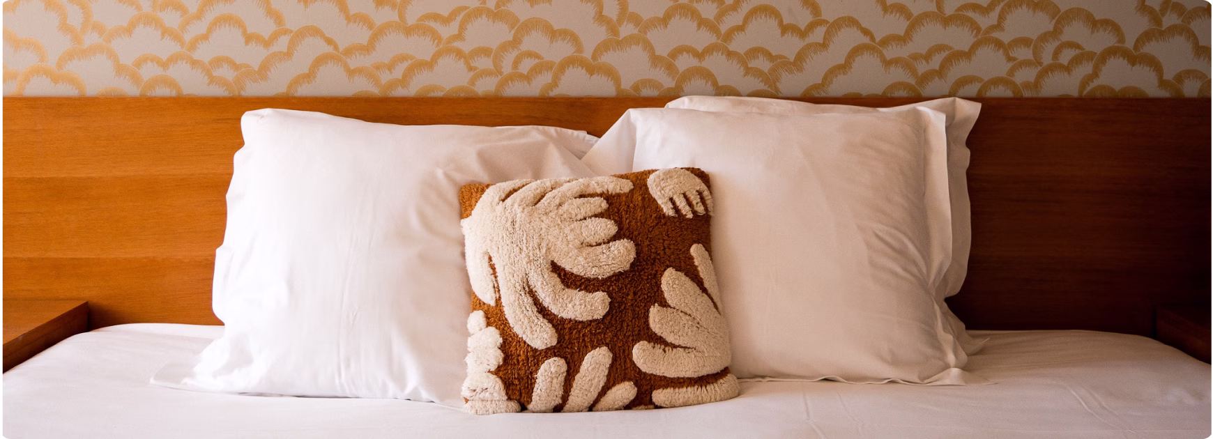 Lit avec deux grands oreillers blancs et un coussin décoratif marron à motifs beiges.