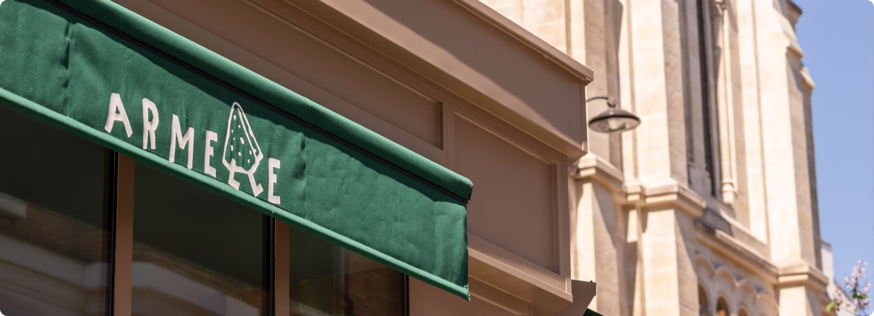 Auvent vert avec le mot « ARMELLE » et une illustration d’arbre dans le bâtiment en arrière-plan.