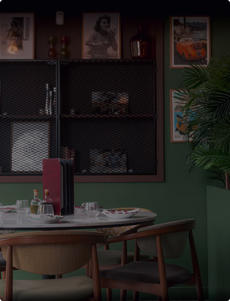 Table ronde avec des chaises en bois, assiettes, verres et condiments dans une salle à manger décorée avec des cadres et une plante verte.