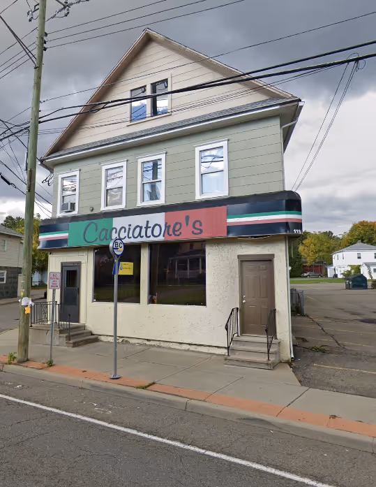 Three-story building with a sign reading 'Cacciatore's' and two doors with small staircases, under a cloudy sky.