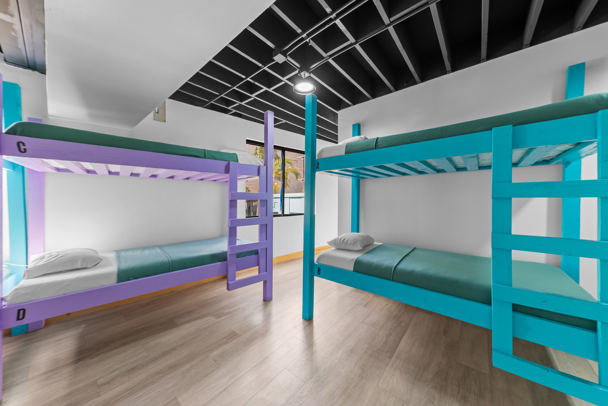 Room with two colorful bunk beds, one purple and one blue, against white walls and wood floor.