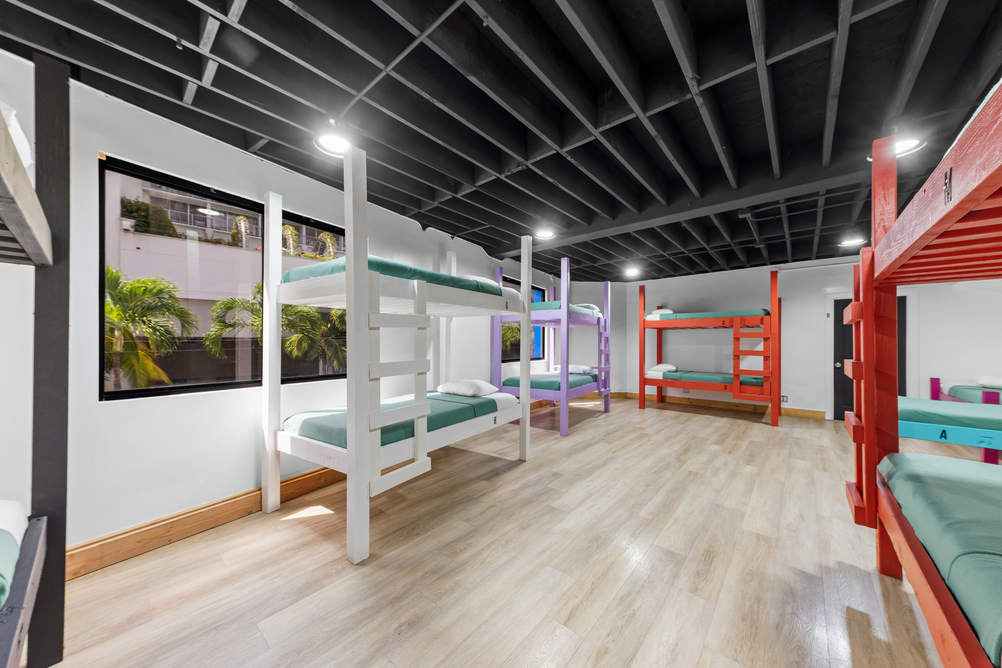 Room with multiple colorful wooden bunk beds arranged on light wood flooring under a black ceiling.