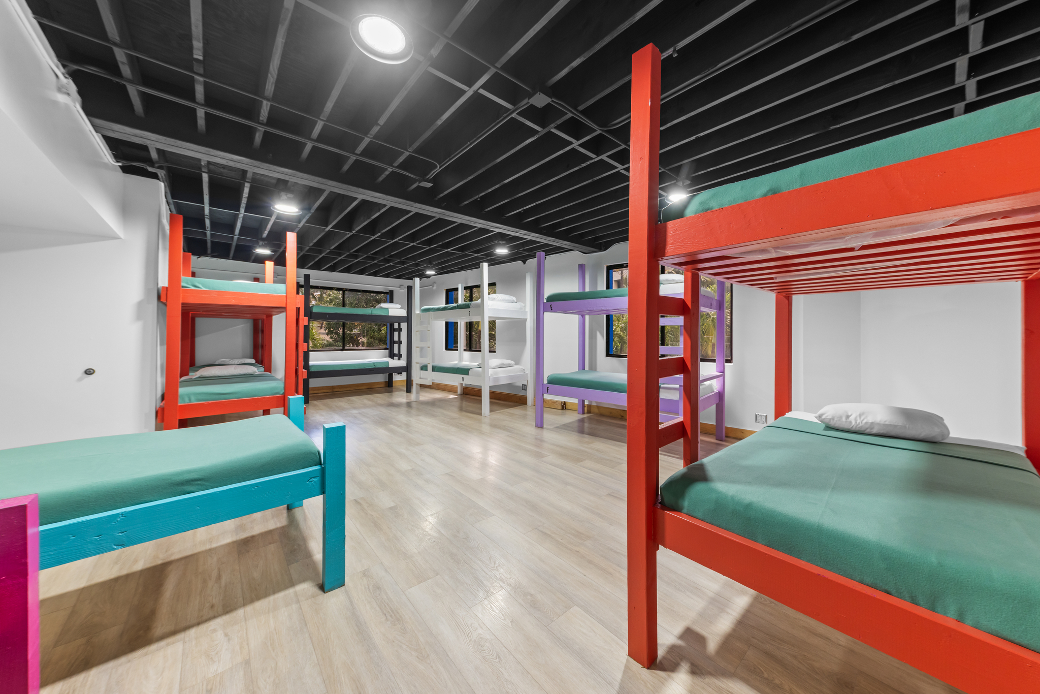 Dorm room with colorful wooden bunk beds and natural light from windows on white walls.