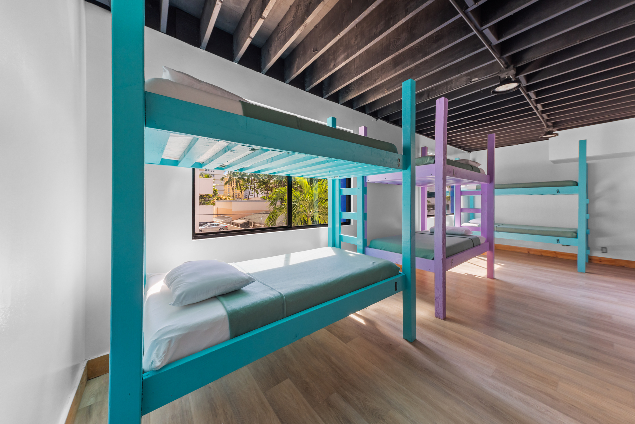 Room with colorful bunk beds near a window showing palm trees outside.