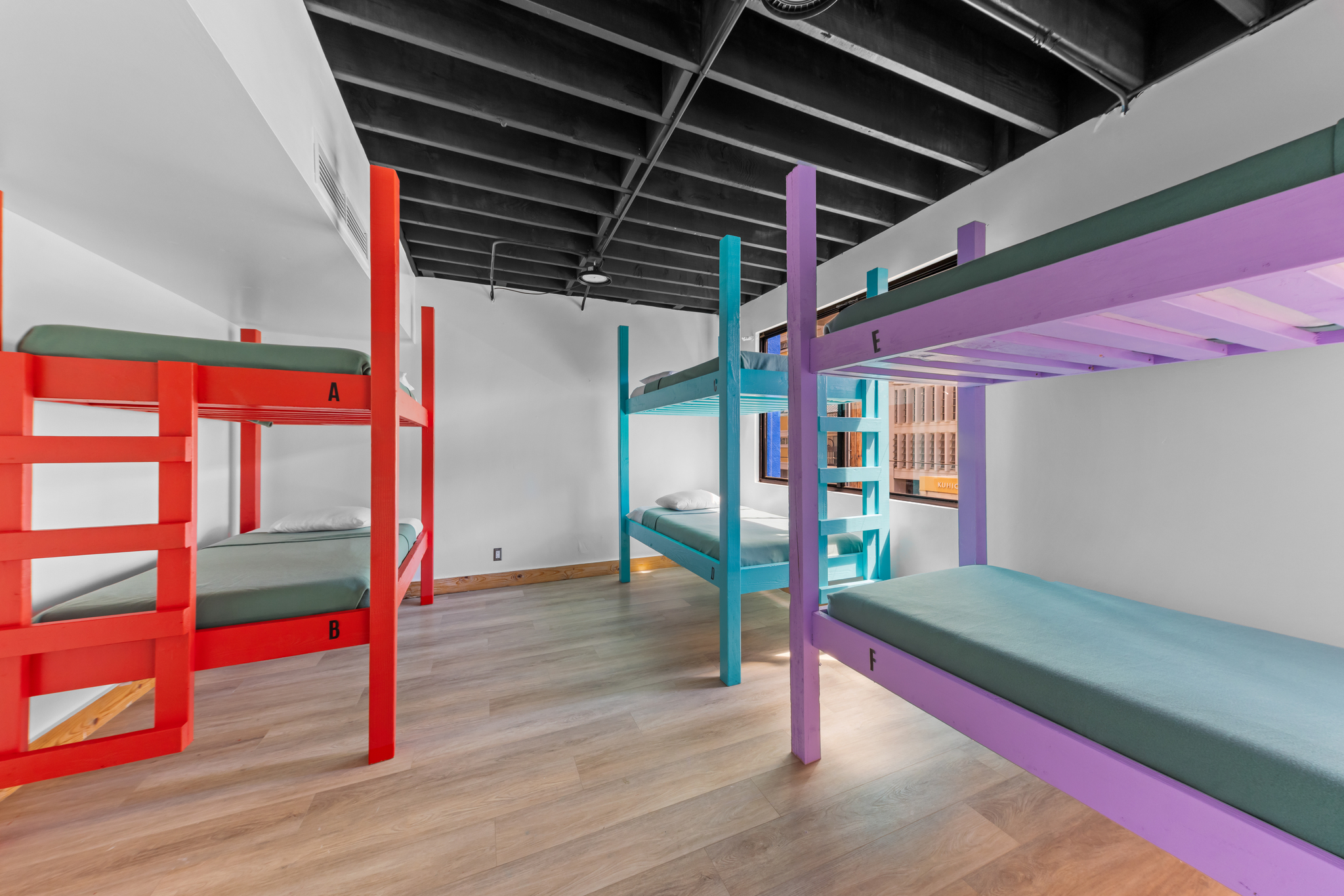 Room with colorful bunk beds in red, teal, and purple with green mattresses and wooden floor.
