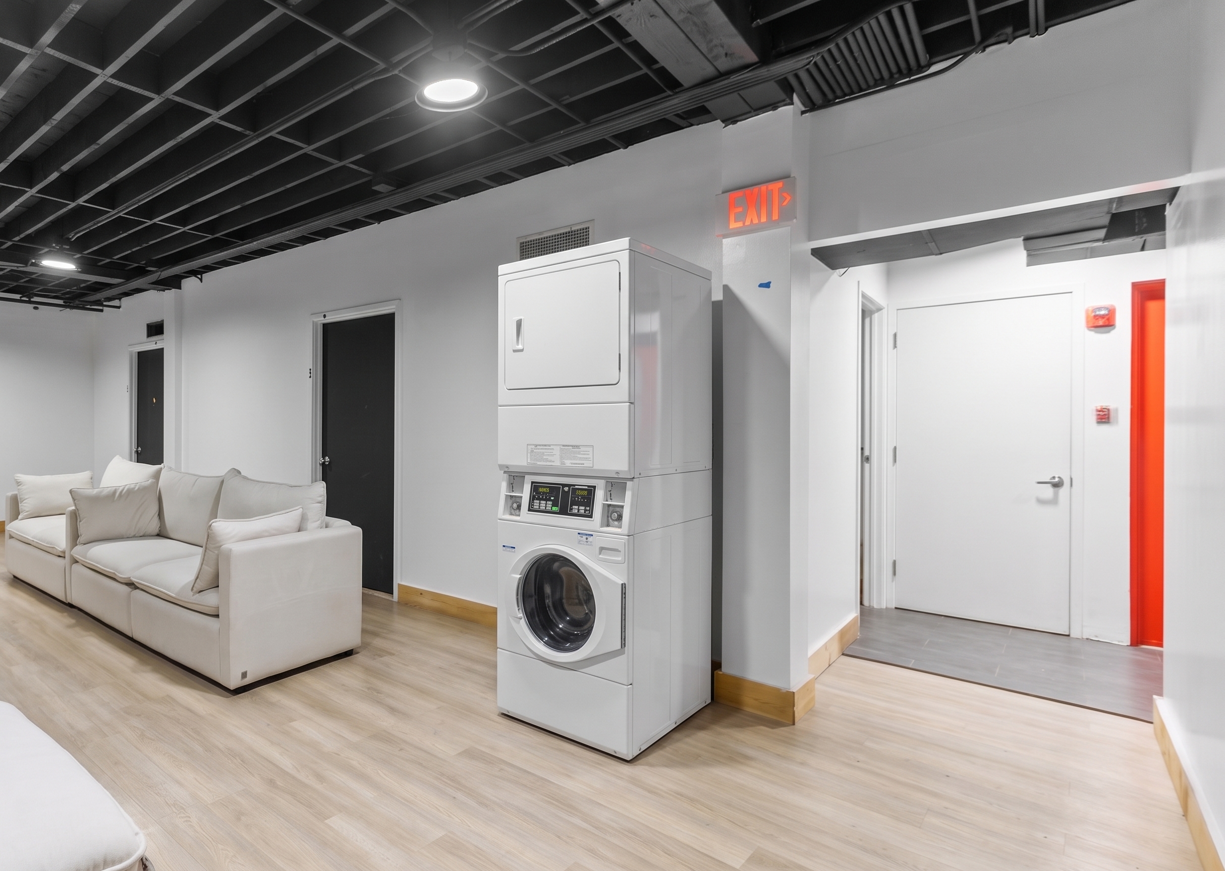 Room with beige sofas, wooden floors, black ceiling beams, a plant, and stacked washer and dryer.