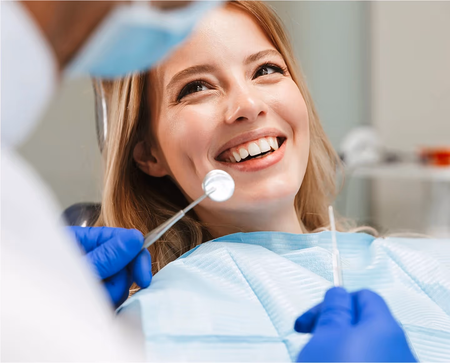 Smiling woman in a dental chair during a dental checkup with dentist holding dental tools.