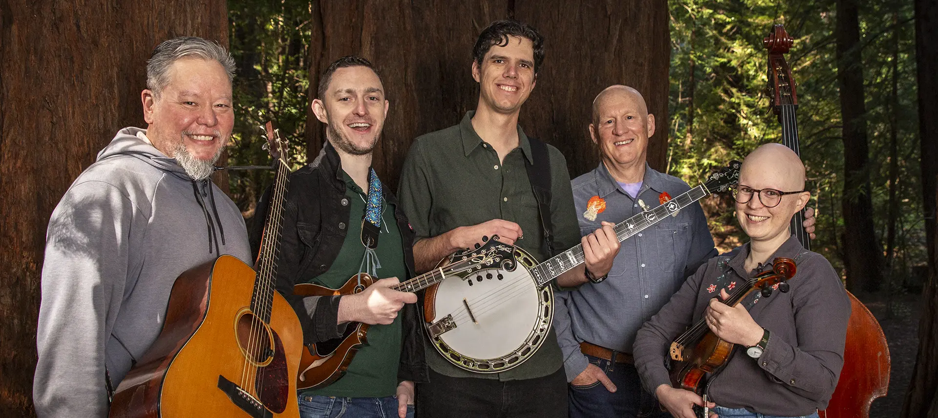 Band members of Critical Grass smiling for a photo next to large redwood trees