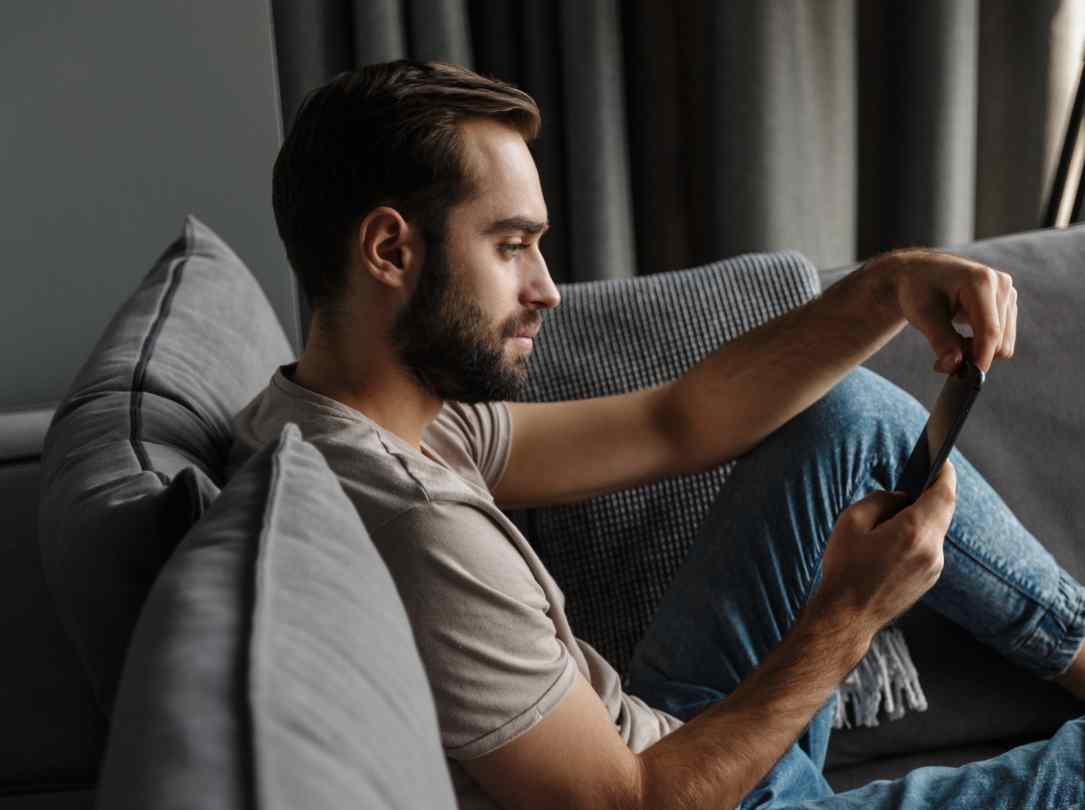 A man looks at his smartphone while sitting on his couch.