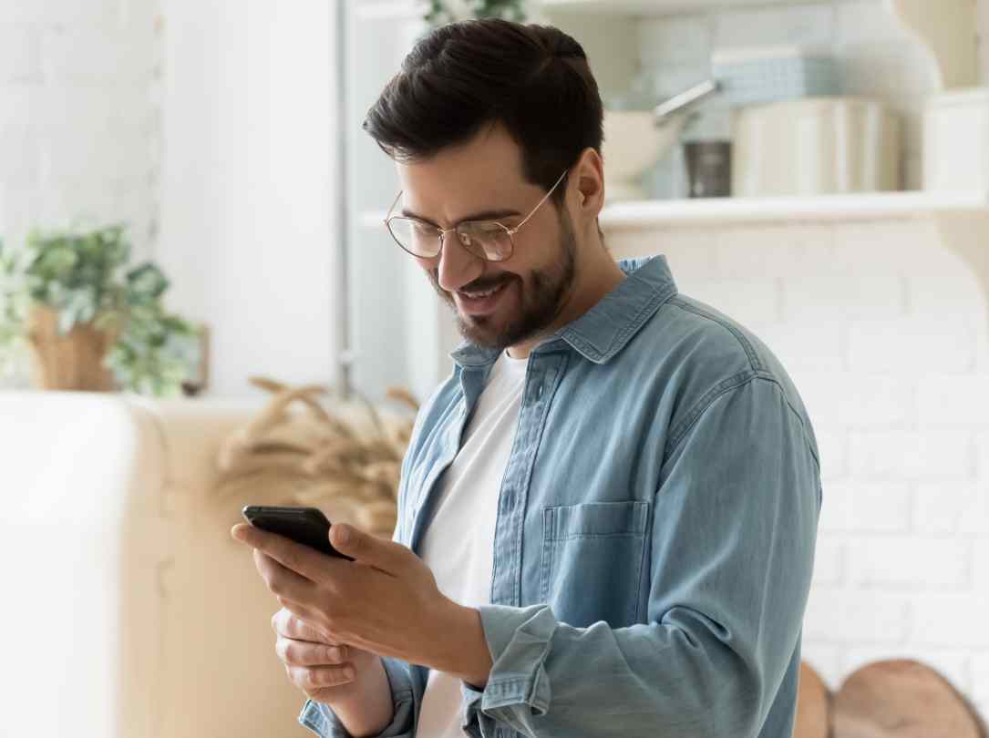 A man smiles as he looks at his smartphone reacting to good news.