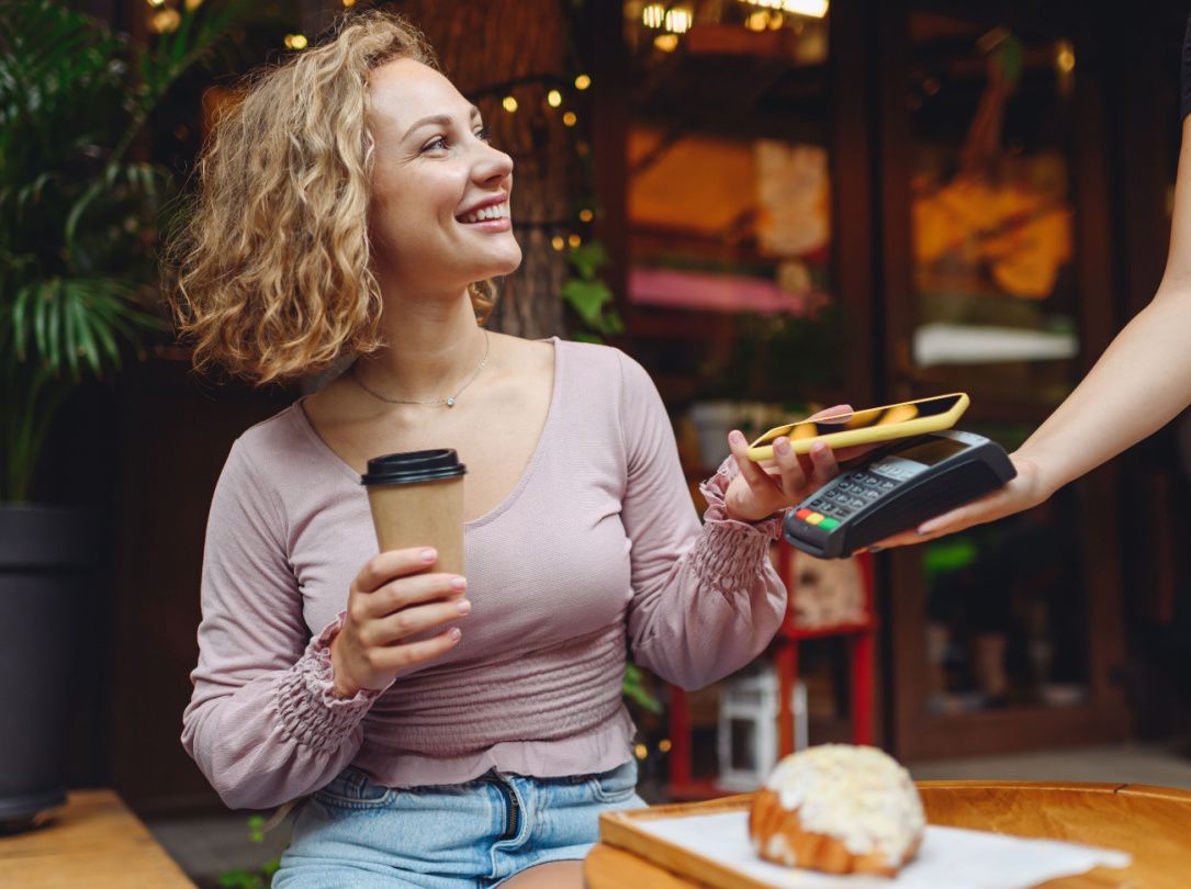 Uma mulher compra seu café tocando o telefone no leitor de cartão.
