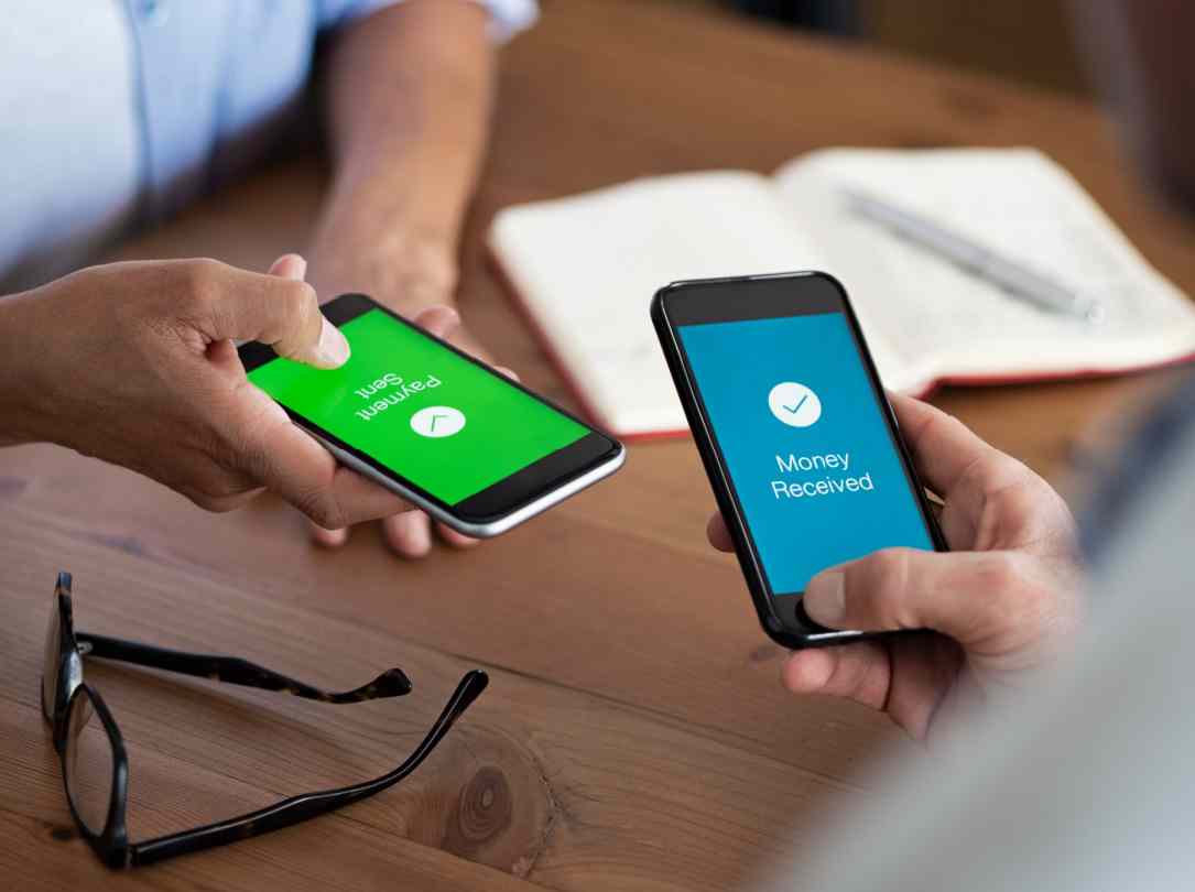 A person sends a payment on their smartphone and another person receives it.
