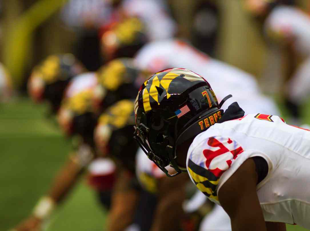 Maryland football player readies himself on the line next to his teammates.