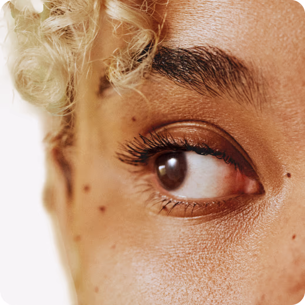 Close-up of an eye with long eyelashes and curly blond hair visible nearby.