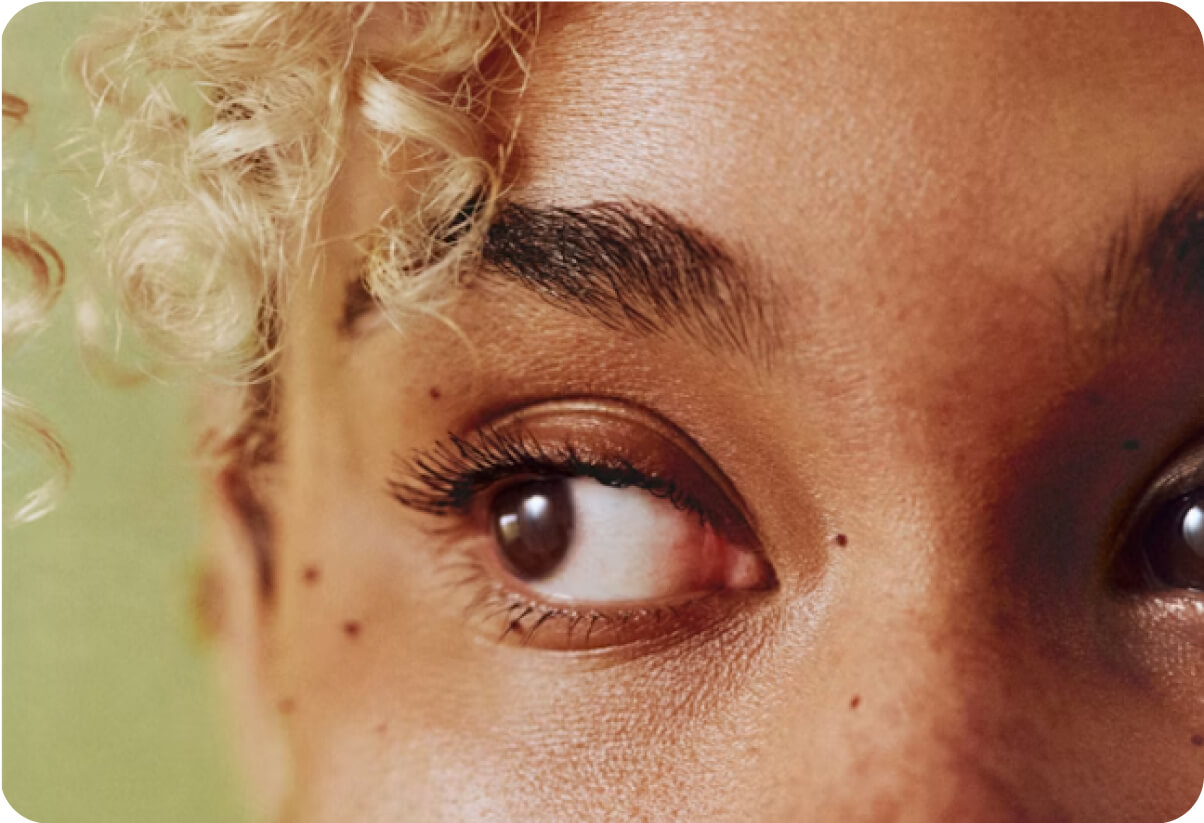 Close-up of a person with light curly hair looking to the side, showing detailed skin texture and natural eyebrows.