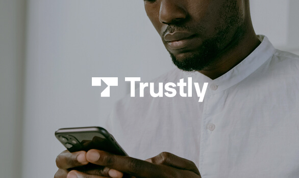 Close-up of a man in a white shirt using a smartphone with Trustly logo overlay.