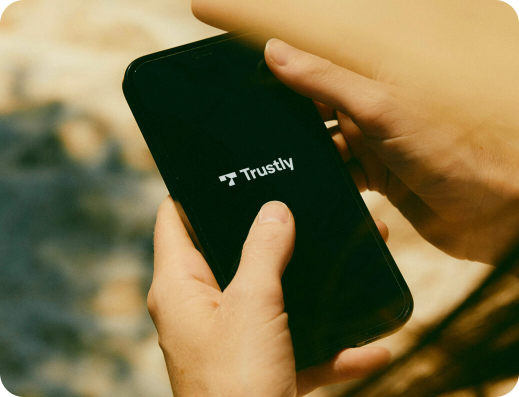 Person holding a smartphone displaying the Trustly logo on the screen.