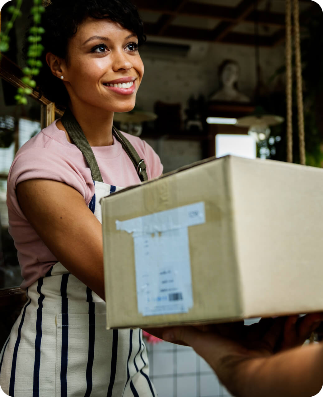 Smiling woman in striped apron handing over a cardboard package indoors.