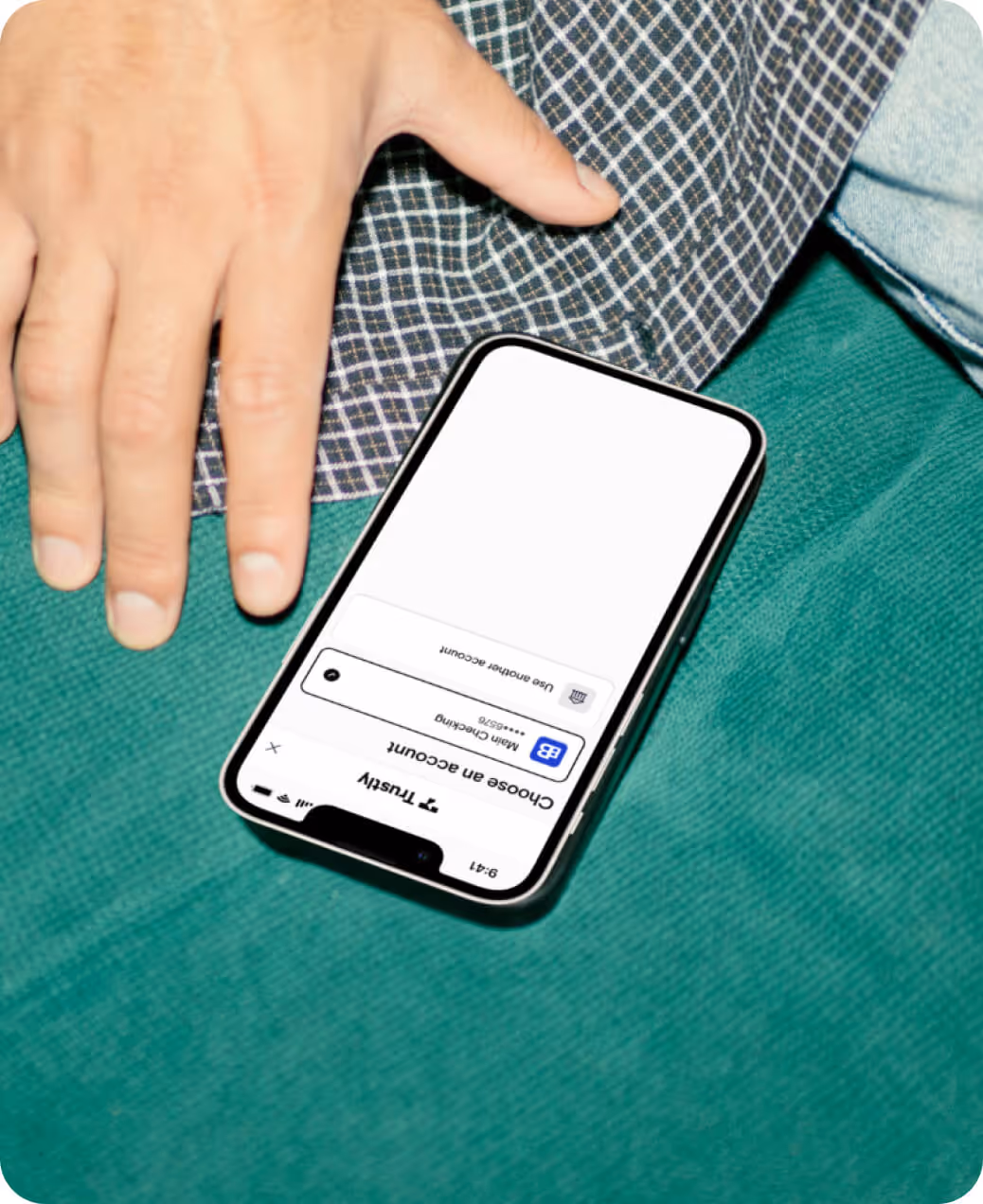 Smartphone showing a login screen for choosing an account with a hand resting nearby on green fabric.