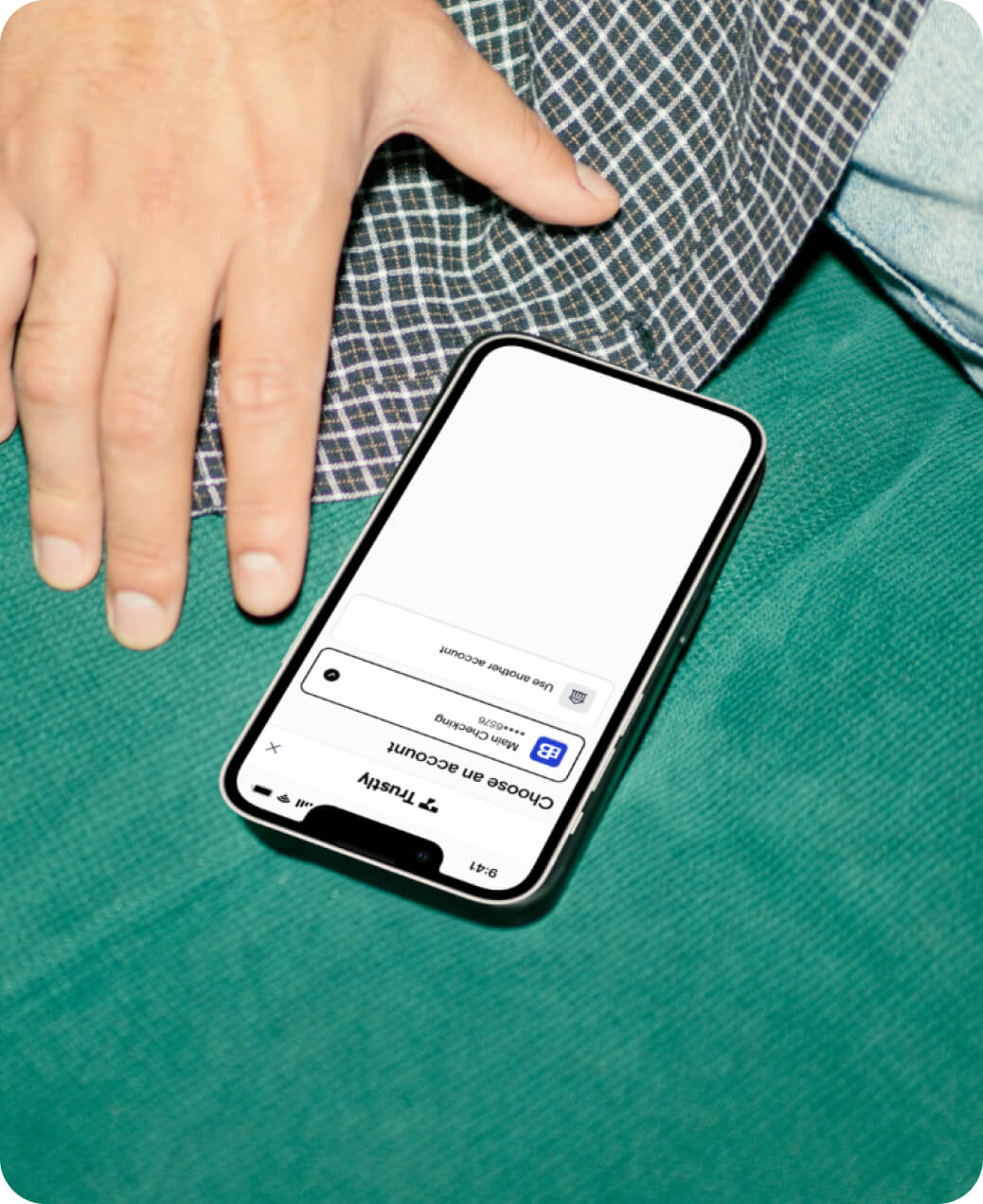 Smartphone showing a login screen for choosing an account with a hand resting nearby on green fabric.