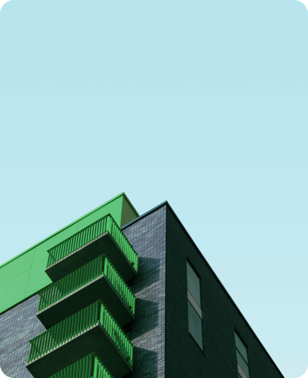 Modern building corner with green balconies and black brick facade against clear blue sky.