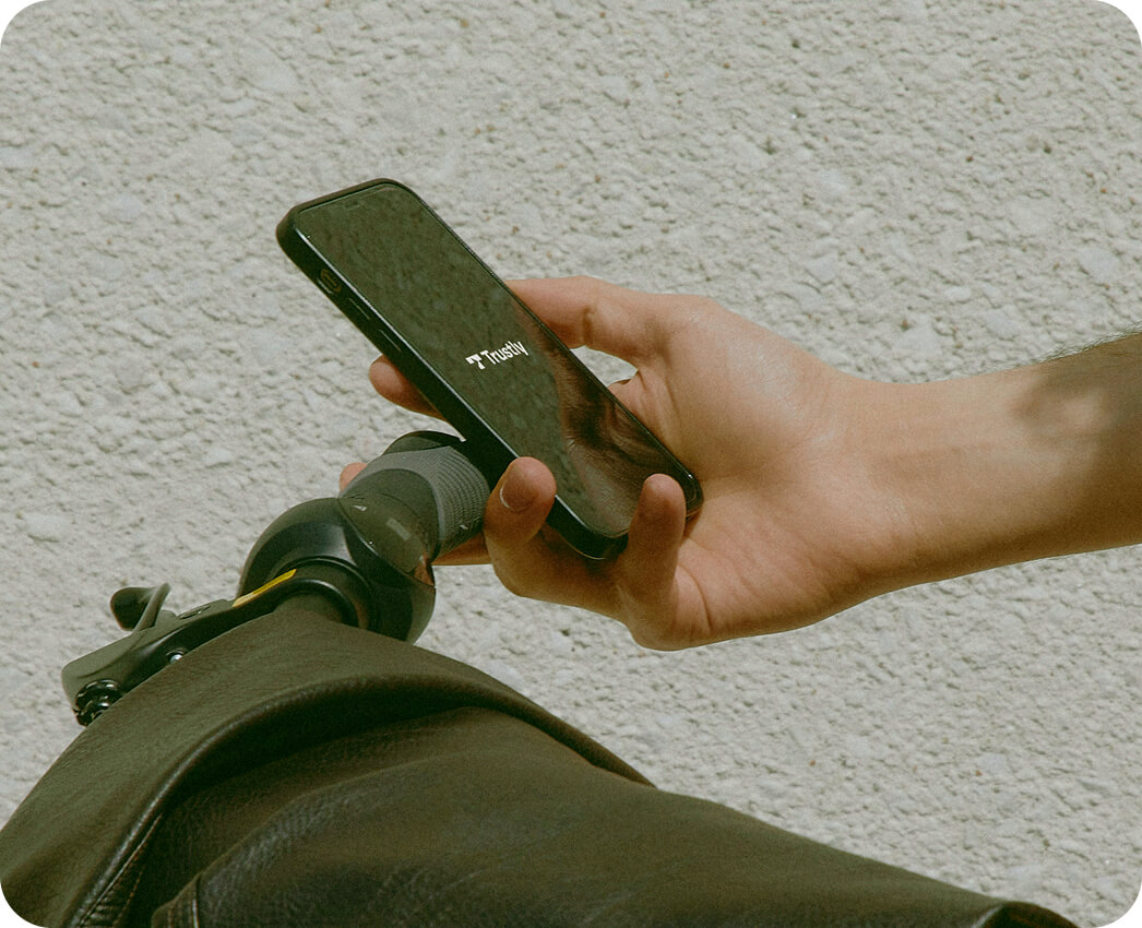 Hand holding a smartphone near a bicycle handlebar against a textured wall.