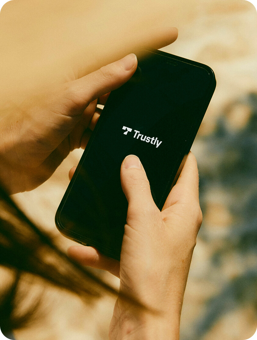 Close-up of hands holding a smartphone displaying the Trustly logo on the screen.