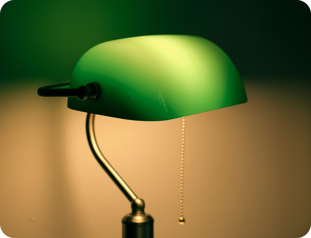 A classic green banker’s desk lamp with a pull chain switch, illuminated against a softly blurred background.