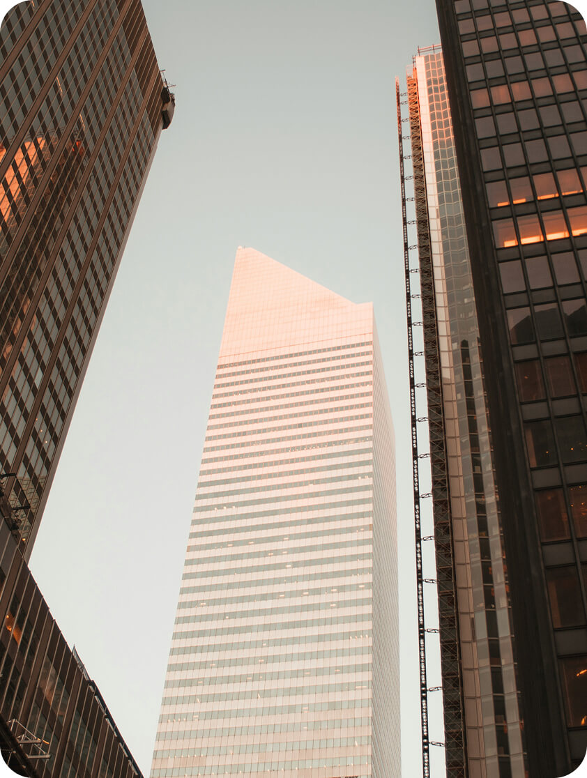 Low-angle view of a tall, modern skyscraper with reflective glass windows during sunset, flanked by two other high-rise buildings.
