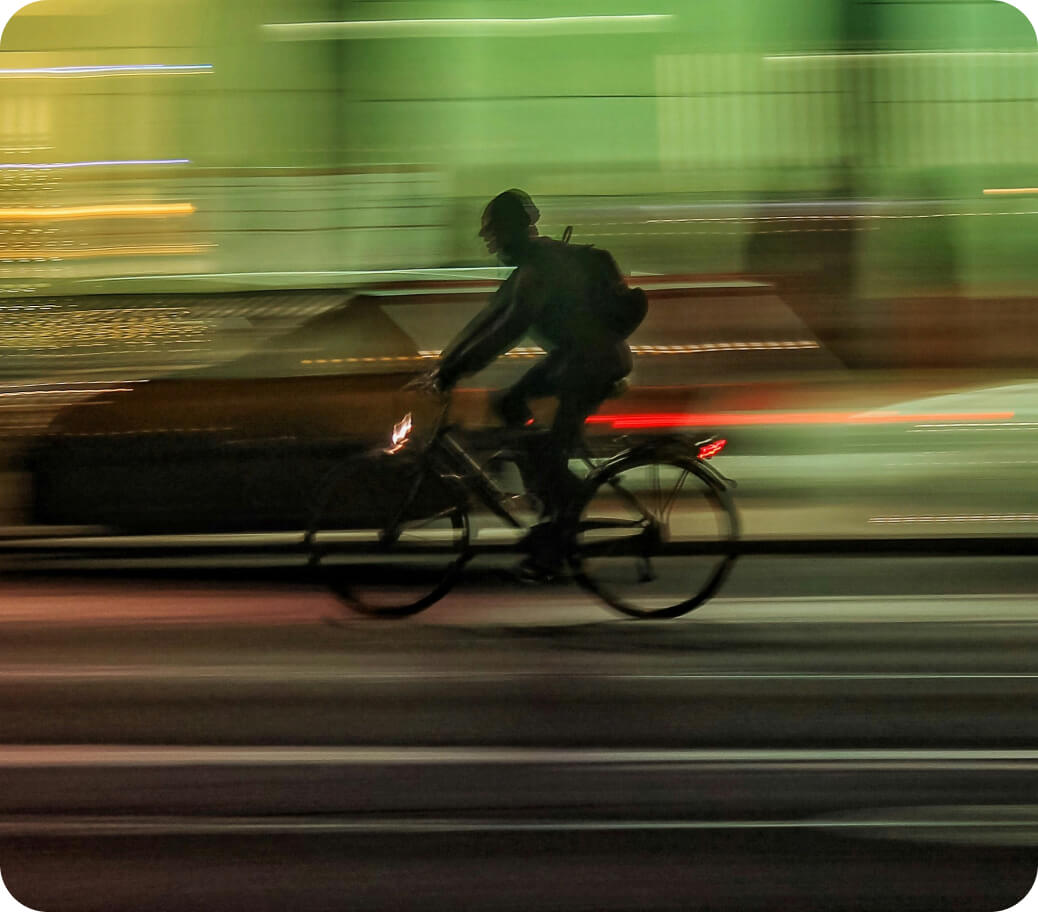 Silhouette of a person riding a bicycle at night with blurred motion lights in the background.