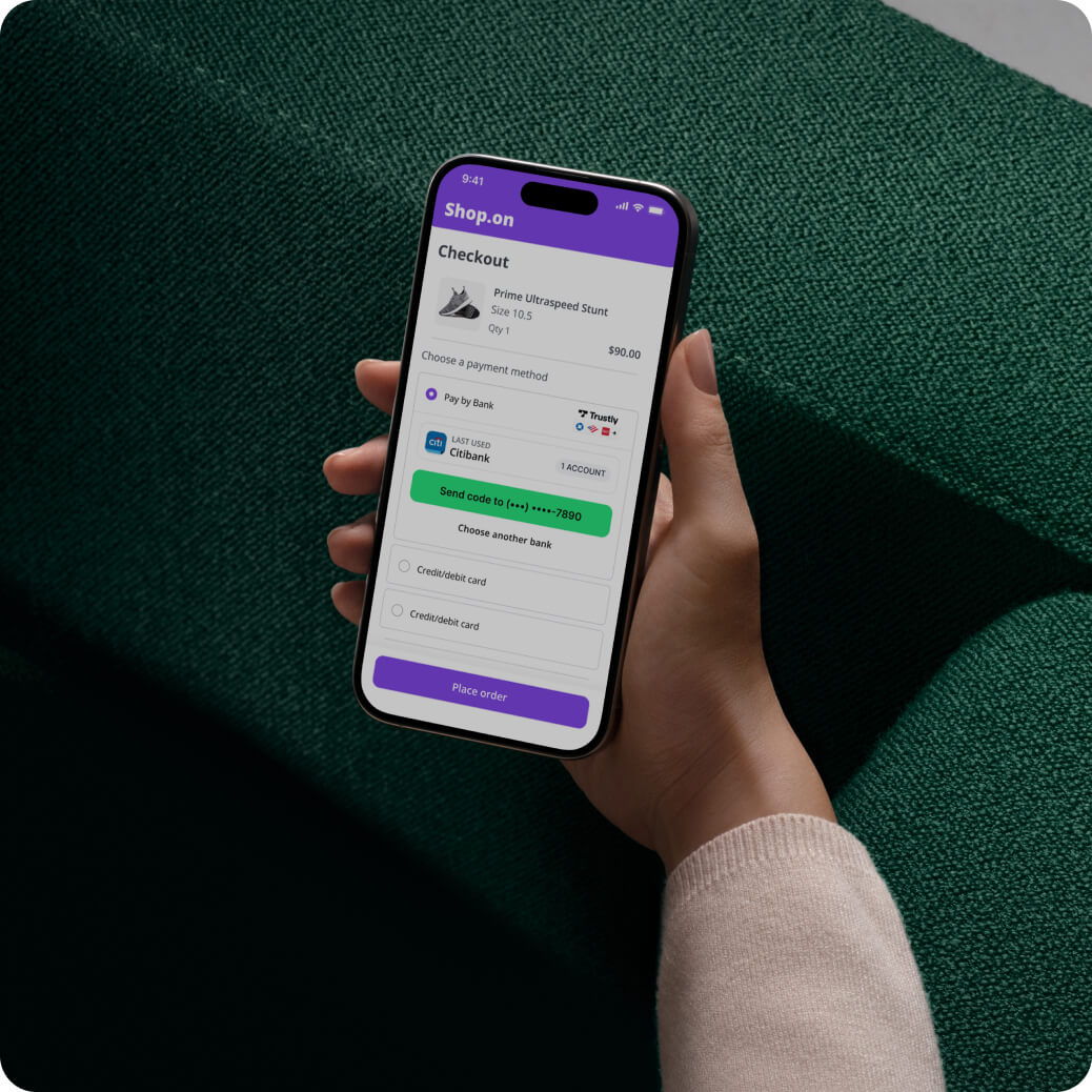 Hand holding smartphone displaying Shop.on checkout screen for purchasing gray sneakers priced at $90 with payment options including bank transfer and credit card.