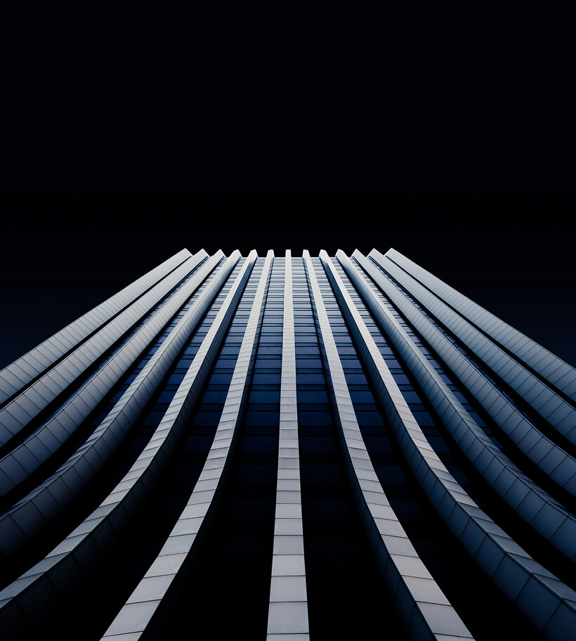 Low-angle view of a modern skyscraper with vertical lines and dark reflective windows against a black sky.