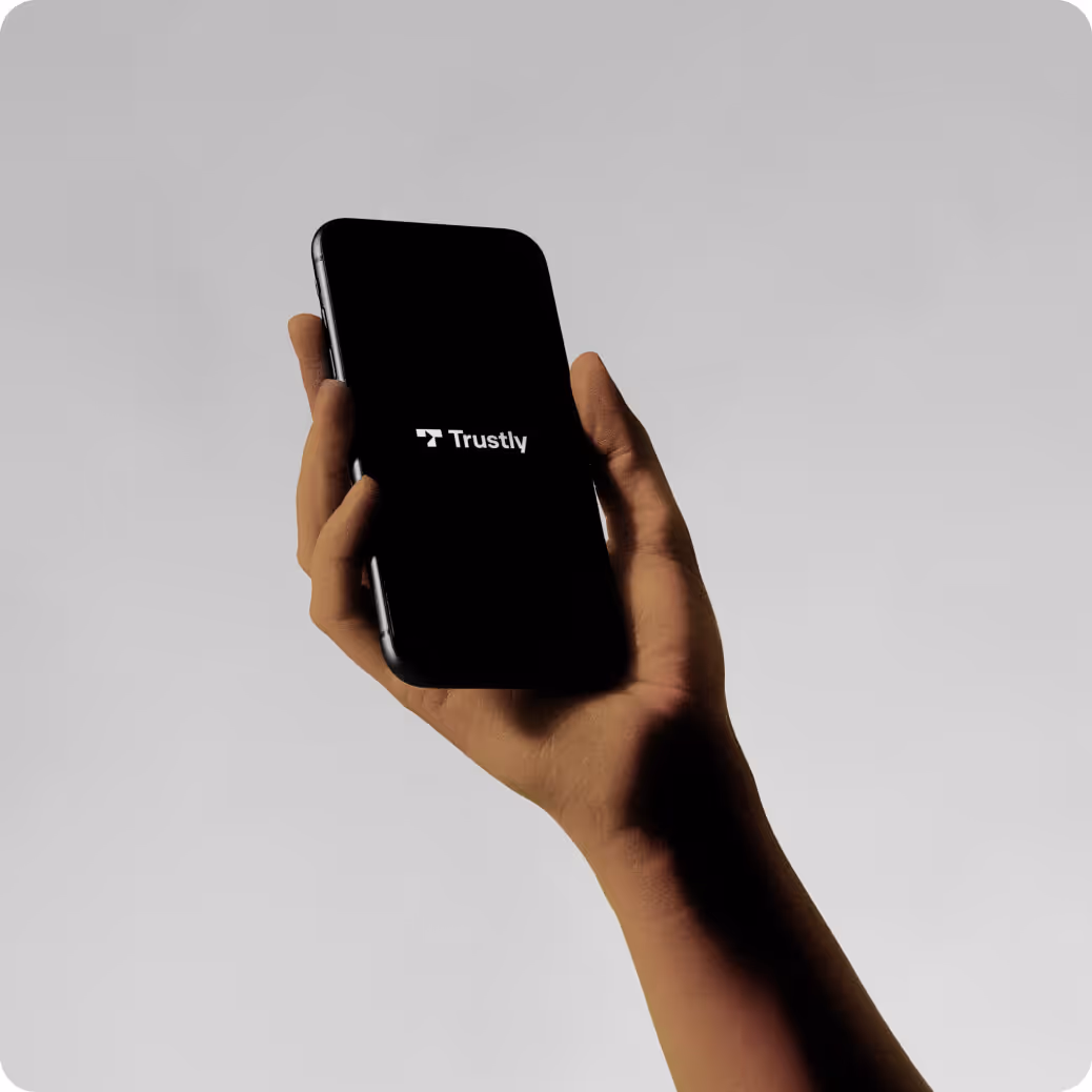Hand holding a smartphone displaying the Trustly logo on a black screen.