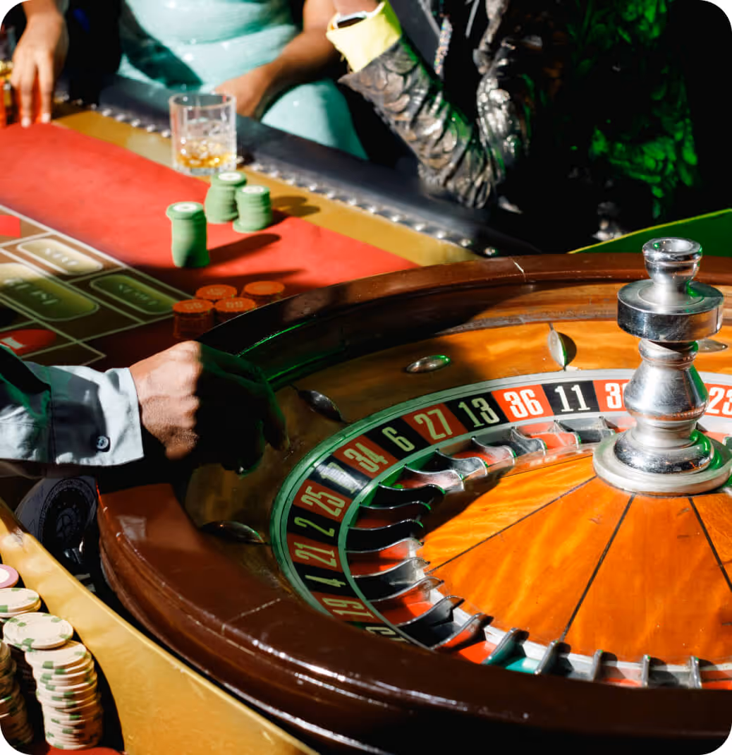 Close-up of a roulette wheel and players' hands with poker chips on a casino table.