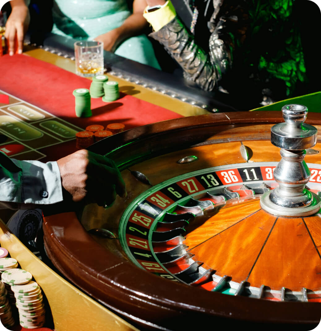 Close-up of a roulette wheel and players' hands with poker chips on a casino table.
