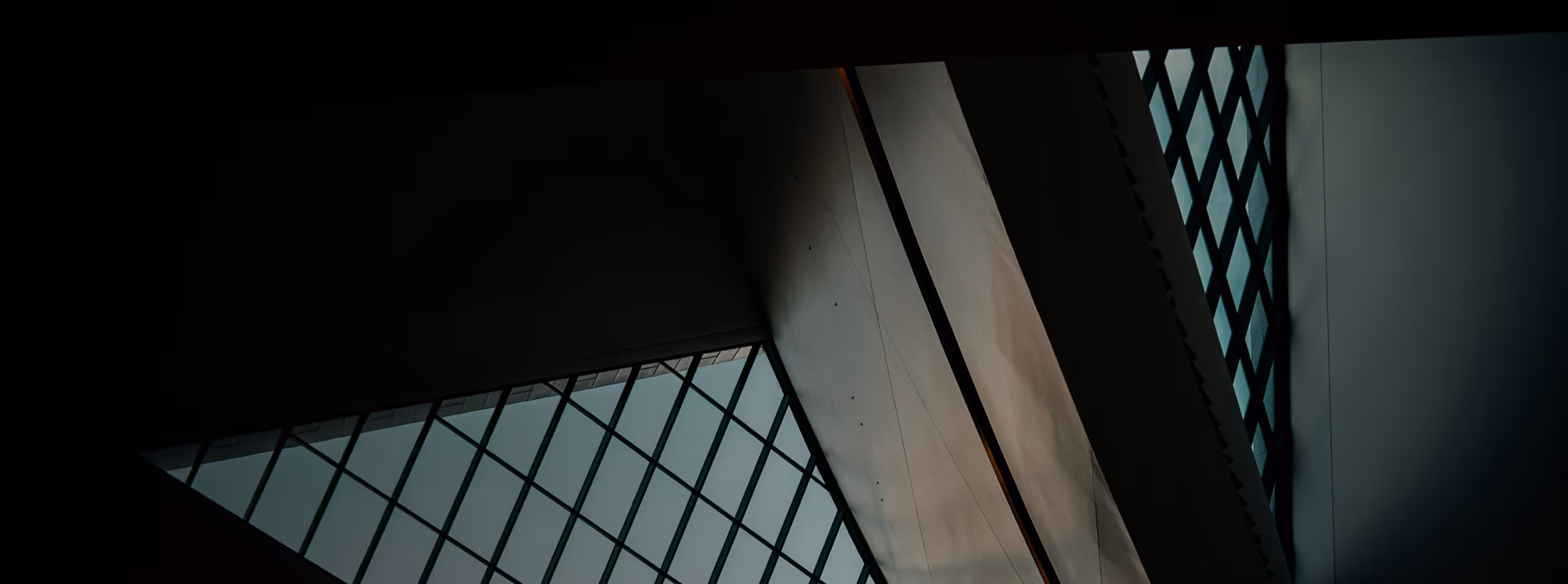 Interior view of a modern building ceiling with large grid-patterned glass windows and angular architectural elements.