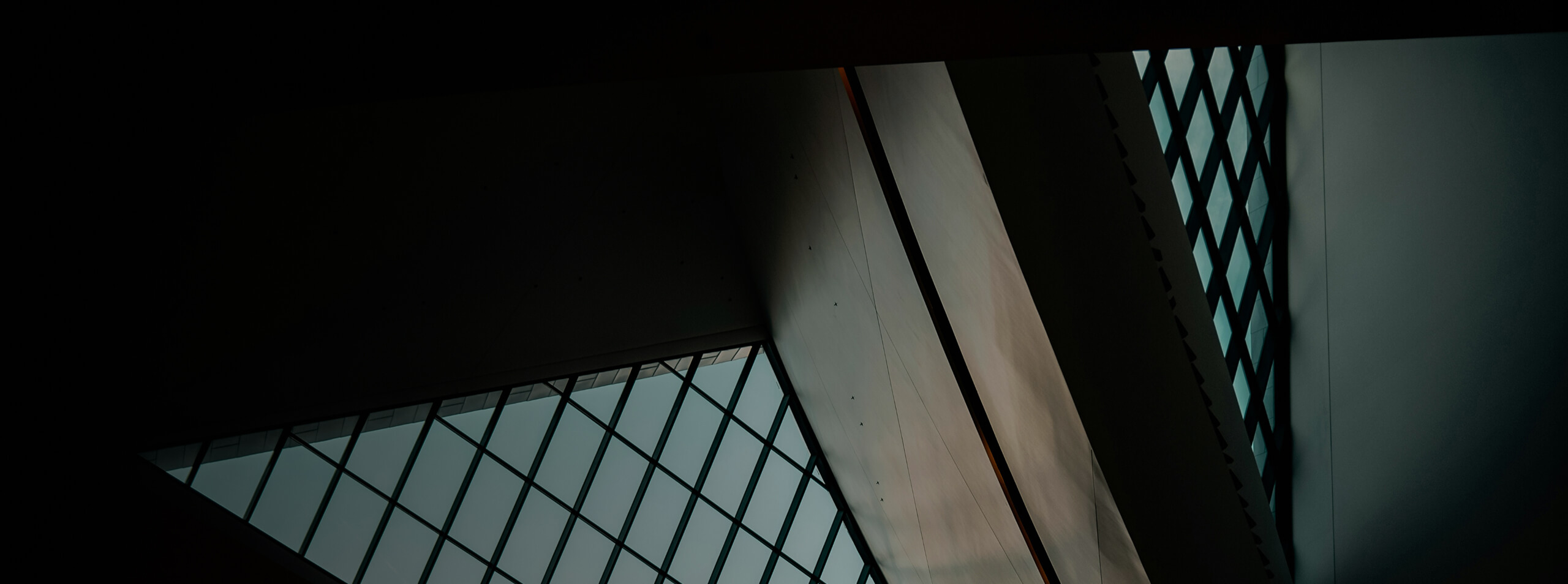 Interior view of a modern building ceiling with large grid-patterned glass windows and angular architectural elements.