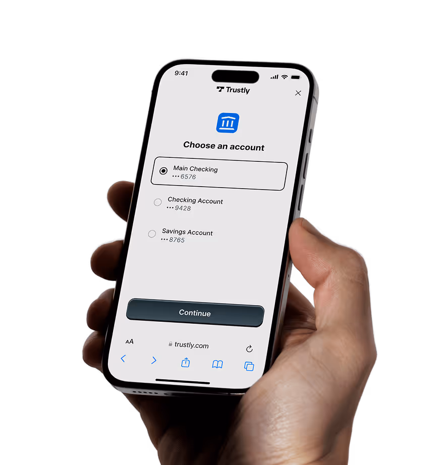 Hand holding smartphone displaying Trustly app screen to choose a bank account with options for Main Checking, Checking Account, and Savings Account.