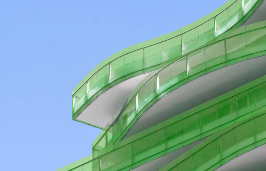 Curved modern building facade with translucent green panels against a clear blue sky.