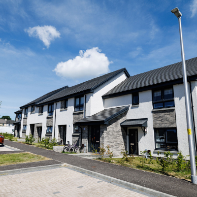 Row of modern white and gray townhouses with pitched roofs under a blue sky with scattered clouds.