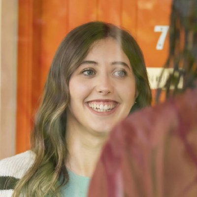 Young woman with long hair smiling through a glass window with an orange background.