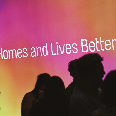 Silhouettes of people in front of a colorful backdrop with white text that reads 'Homes and Lives Better'.
